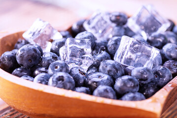 Freshly picked blueberries with ice cubes in a heart-shaped wooden plate