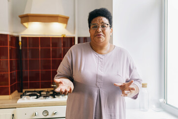Indoor image of mature housewife or grandma of african ethnicity standing against kitchen gas stove...
