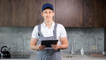 Smiling man plumber inspects records on clipboard standing in modern kitchen. Specialist work done. Provision of services in plumbing sphere