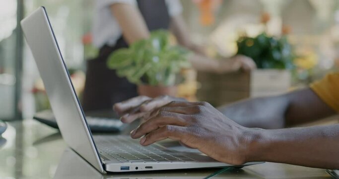 Close-up of male hands using laptop typing while man working in flower shop at counter. Modern technology and successful entrepreneur concept.