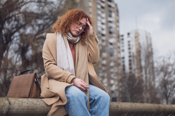 Natural portrait of a caucasian ginger woman with freckles and curly hair. She is overworked and having headache.