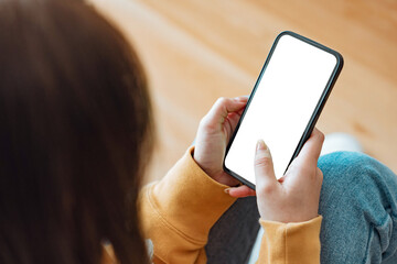 Hand of woman touching mockup blank screen mobile smartphone on sofa at home, White empty space for advertise text.