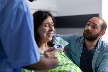 Pregnant woman holding hand of nurse and husband in hospital ward, having painful contractions. Patient with pregnancy getting into labor having medical assistance at healthcare facility. Close up
