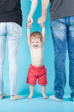 Laughing Caucasian Kid With Positive Facial Expression Hanging on Parental Hands Together Against Blue