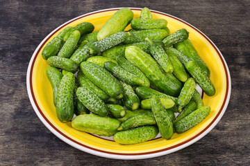 Fresh washed cucumbers and gherkins on dish on black surface