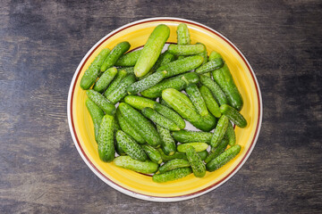 Cucumbers and gherkins on dish on black surface, top view