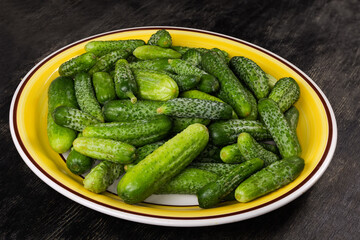 Fresh washed cucumbers and gherkins on dish on black surface