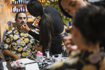 Halloween party hairstyle and makeup preparations, make-up artist making up a man with white paint