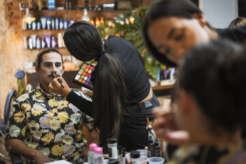 Halloween party hairstyle and makeup preparations, make-up artist making up a man with white paint