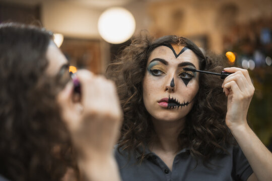 Halloween party hairstyle and makeup preparations, woman fixing her eyelashes looking in the mirror