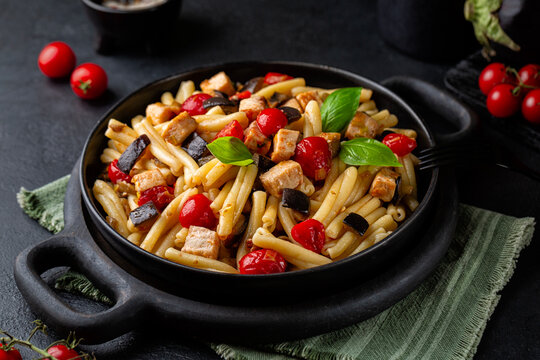 Sicilian pasta, casarecce with swordfish, tomato, and eggplant. Decorated with basil leaves. Dark table surface.