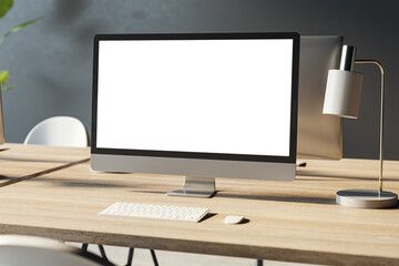 Close up of empty white computer monitor on wooden office desktop with lamp and supplies. Designer workplace concept. Mock up, 3D Rendering.