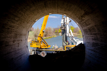 Look through pipe on mobile crane and drilling machine working together on bridge foundation