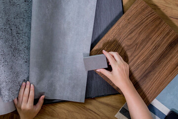 An interior designer's hand selects a palette of sample materials that includes different types, textures and colors of artificial stone, wooden MDF board and decorative wallpaper
