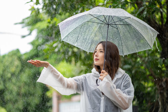 Its raining down hard. Shot of a young asian woman standing in the rain with an umbrella.