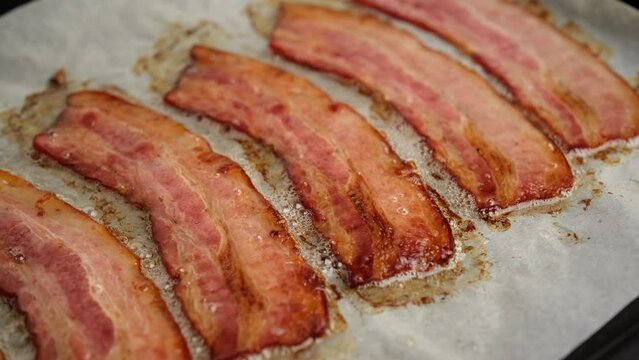 Frying bacon slices in oven, slider shot. Crispy pieces of fried delicious bacon. Traditional breakfast