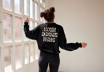 Mockup of woman wearing sweatshirt with customizable color by window view with arms out