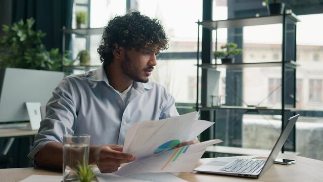 Stressed sad Arabian Indian man anxious male worker executive manager working at office check paperwork commerce on laptop upset businessman hold business papers financial mistake debt problem despair