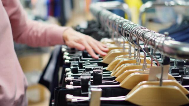 Women's hands gently touch men's trousers hanging on hangers in the store.