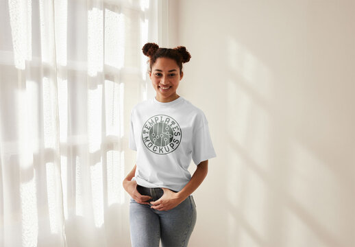 Mockup of woman wearing customizable t-shirt by window, hands on waistband