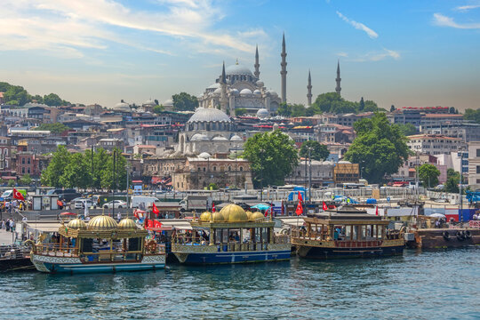 View of the central historical part of Istanbul with old buildings and a large mosque on a hill, traditional decorative boats and piers, ships and ferries with people floating in the Bosphorus.