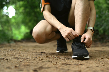 Unrecognizable male runner tying shoes laces, getting ready for trail run in forest. Sports,...