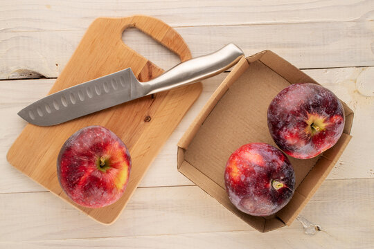 Four ripe juicy red apples with paper plate, wooden kitchen board and knife on wooden table, macro, top view.