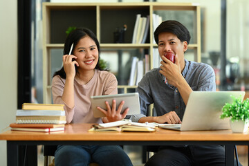 Two college students using digital tablet in library, studying together for exam or research for project