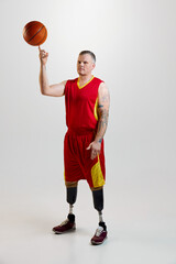 Fototapeta premium Attractive, confident, sporty man with prosthetic legs, disability in uniform spins basketball ball on finger. Inclusive sport for people with disabilities.