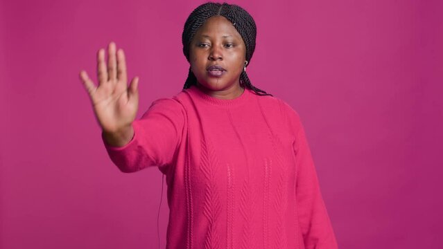 African american lady with denying using stop hand gesture towards camera against isolated background. Female fashion influencer disapproving rejecting disagree portrait on pink background.