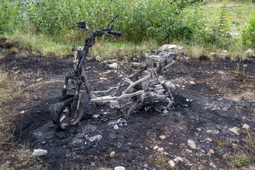 Burned electric scooter with green grass in the background insurance concept