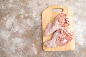Raw turkey wing on a wooden cutting board on a brown concrete background. Top view, copy space.
