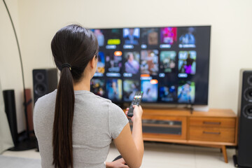 Woman watch TV and use remote control for choosing program at home
