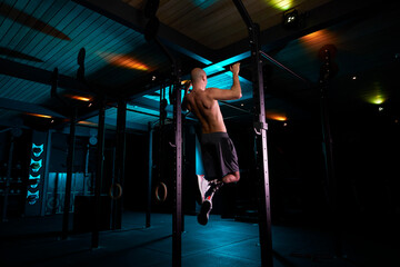 Shirtless young man with prosthetic legs doing pull ups in gym