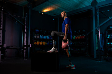 Young man with prosthetic legs working out with kettlebells in gym