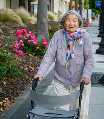 Front view of a smiling senior woman walking outdoors with her walker. Vertical shot.
