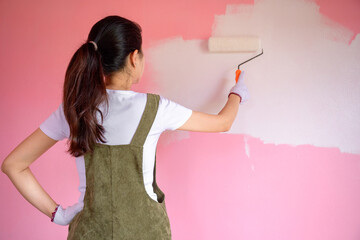 Back view of young asian woman painting house wall with roller brush while renovating the house Rear view of woman painting wall with roller and renovating repair and decoration concept
