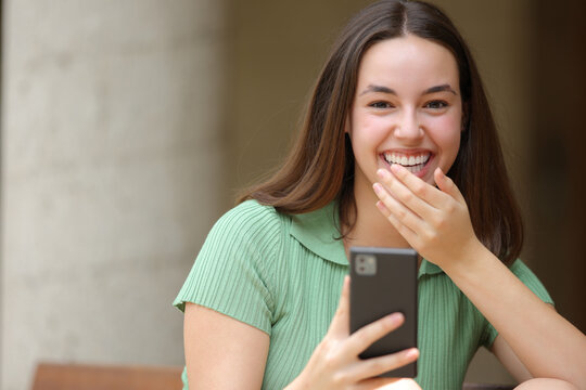 Happy woman laughing holding phone in the street