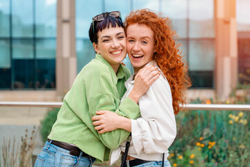 Fototapeta premium smiling young women girlfriends having a fun time together, talking and using phones at outdoor in urban city. people, communication, friendship and lifestyle concept