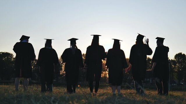 Silhouettes of college graduates waving their caps at sunset.