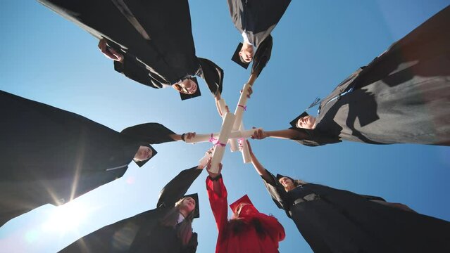 College graduates join hands with their diplomas. The concept of friendship.