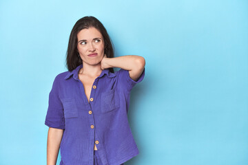 Fototapeta premium Young caucasian woman on blue backdrop touching back of head, thinking and making a choice.