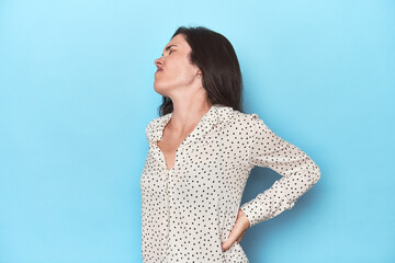 Young caucasian woman on blue backdrop suffering a back pain.