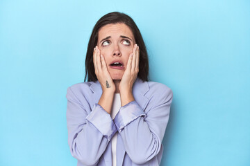 Woman in blue blazer on blue background whining and crying disconsolately.