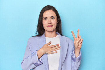 Woman in blue blazer on blue background taking an oath, putting hand on chest.