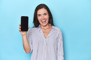 Fototapeta premium Woman displaying phone screen on blue backdrop