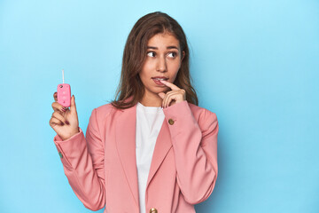 Teen girl in pink, proudly holding her car key relaxed thinking about something looking at a copy space.