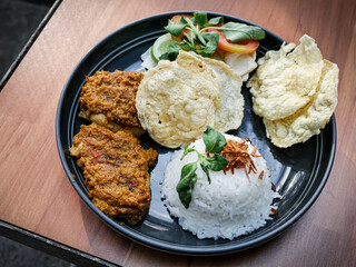 Ayam bakar Taliwang is a traditional roast chicken from Lombok Indonesia, isolated on a wooden background, served with vegetables. Spicy but tasty cuisine