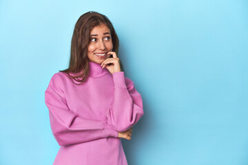 Teen girl in cozy pink sweatshirt on blue relaxed thinking about something looking at a copy space.