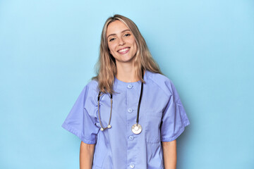 Young caucasian nurse in blue studio happy, smiling and cheerful.